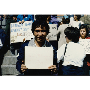 Demonstrator stands on the steps of the Massachusetts State House at a rally for bilingual education holding a protest sign