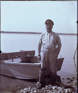 Man standing by boat on the beach, Mashpee, Mass.