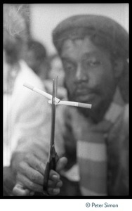 Peter Tosh holding up two cigarettes with scissors, surrounded by a haze of marijuana smoke, backstage at Saturday Night Live
