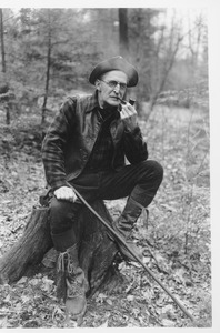 Charles Hiram Thayer seated on a tree stump smoking a pipe