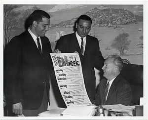 Two unidentified men present NEAA week poster to Mayor John F. Collins