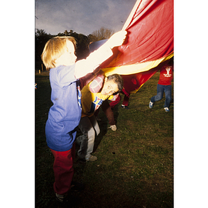 Young children pulling on a large red tarp