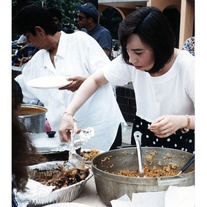 Women serve food outside during a neighborhood festivity.