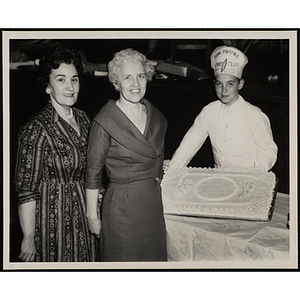 Two women and Tom Pappas Chef Club member pose with a decorated cake at Mothers' Club event