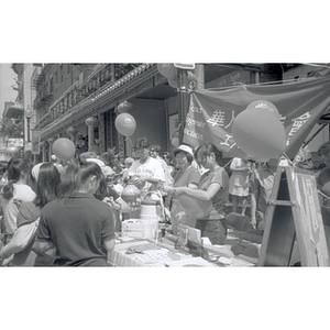 Woman and others distribute balloons at Chinese Progressive Association's booth at Boston Chinatown's August Moon Festival