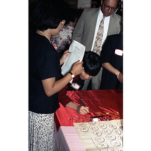 Guests sign a banner during Chinese Progressive Association's 15th Anniversary Celebration while Suzanne Lee looks on