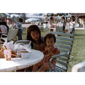 Young girl sits with a toddler in an outdoor eating area