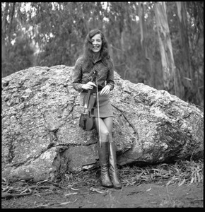 Woman playing a fiddle, posed on a granite boulder in a eucalyptus grove