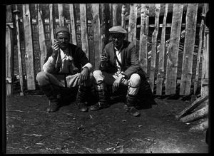 Joseph Obrebski and man, seated by a fence, smoking [no caption]