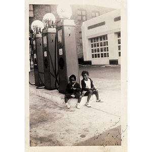 Two young girls sit in front of a Shell gas station