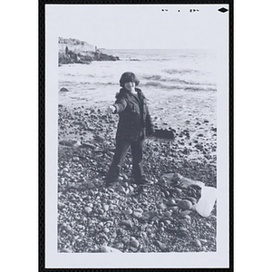 A boy holds out a stone on a beach