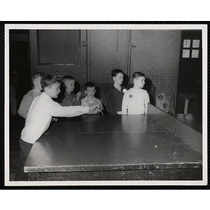 A boy plays table tennis as a group of boys looks on