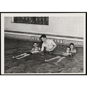 A man instructs boys swimming in a natatorium pool