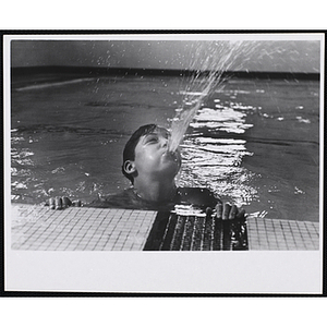 A boy blows water from his mouth as he wades in a natatorium pool