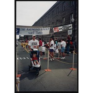 A man pushing a child in a carriage runs past spectators during the Battle of Bunker Hill Road Race