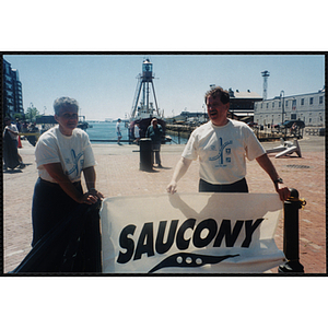 A woman and man stand behind a Saucony banner at the Battle of Bunker Hill Road Race