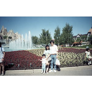 Family stands together in front of a flowerbed and fountain in a botanical garden