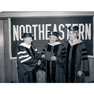 President Kenneth Ryder, left, congratulates honorary degree recipient, George Kariotis, center