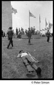 Man lying on the grass near the Washington Monument, with protesters assembling in the background during the March on the Pentagon (mobilization on Washington)