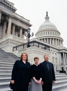 Three people posed on the steps of the United States Capitol building