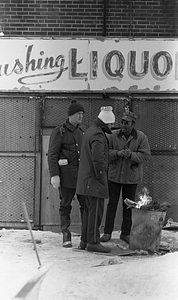 Unidentified men warming themselves by fire in trash can