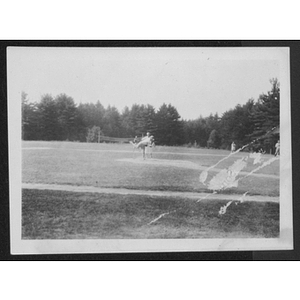 View of baseball field and trees with pitcher throwing on the mound