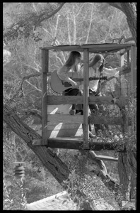 Joni Mitchell playing a guitar, seated in her tree house in Laurel Canyon with Judy Collins