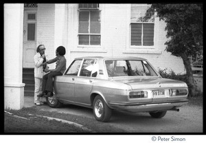 Bob Marley seated on the hood of a car, talking with an interviewer