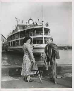 Woman and man with crutches stand before boat