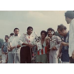 The Marshal stands with three people with large trophies at the Festival Puertorriqueño