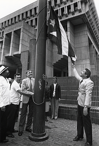 Mayor Raymond L. Flynn, Alfredo de Jesús and two unidentified men raising the Puerto Rican flag outside Boston City Hall while others look on