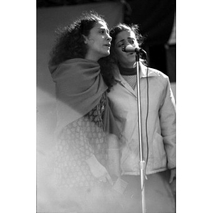 Three-quarter length portrait of two Hispanic women singing into a microphone and performing at a Latino street festival