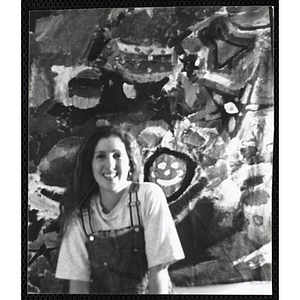 A young woman posing in front of a painting hung on the wall
