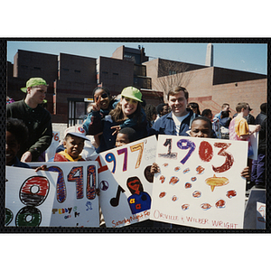 A man and a woman with a girl on her back pose with four boys holding their parade signs at the Boys and Girls Clubs of Boston 100th Anniversary Celebration Parade