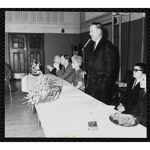 A man speaks into a microphone at the head table during a Dad's Club banquet