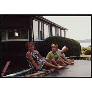 A Girl and two boys sitting outside on a trampoline