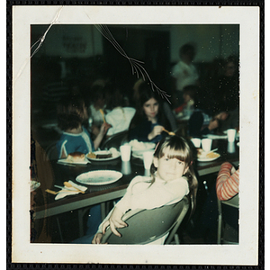 A girl looks at the camera while sitting at a table with food during a South Boston Boys' Club event