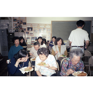 Association members sit in folding chairs eating dinner