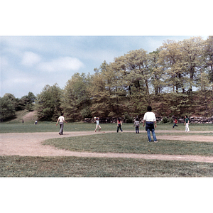 Association members stand on a ball field while one player throws a kickball