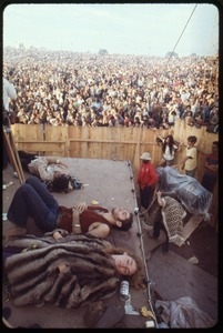 Woman in a fur coat, sleeping on the stage at the Woodstock Festival, with the audience in the background