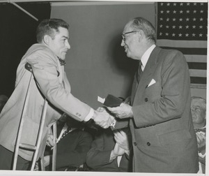 Jeremiah Milbank Sr. shaking hands with a man using crutches