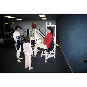 Man sitting on exercise machine as woman and child watch