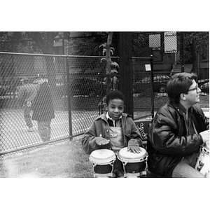 Young boy in a playground playing bongo drums alongside Alex Alvear.