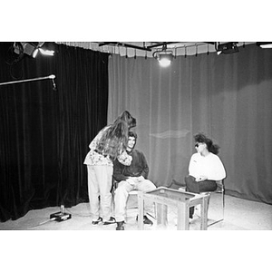 Young woman attaching a microphone to a young man on the set of Villa Victoria's public access television station.