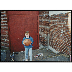 A girl with face paint holds a basketball at a carnival