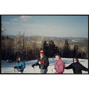 Three teenage girls and a man pose for a group shot at the top of a ski slope