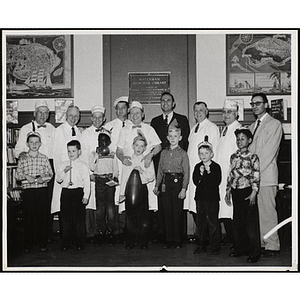 Roxbury Clubhouse Committee overseer and chairman George E. Putnam (4th from right), Clubhouse Committee's L.M. Peters (3rd from right), and seven other men pose with a group of boys at a Midget birthday party event during Boys' Club Week, 1-7 April 1957