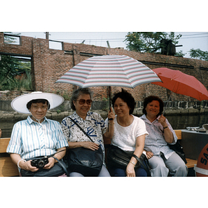 Four women sit on a ferry boat and hold umbrellas while smiling
