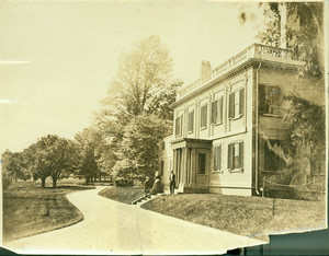 Exterior view of the Lyman Estate "at early stage," Waltham, Mass. Three people are standing on the front steps.