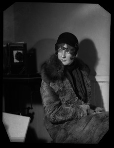 Mae Houston: portrait in a winter coat and cloche hat, large view camera in the background